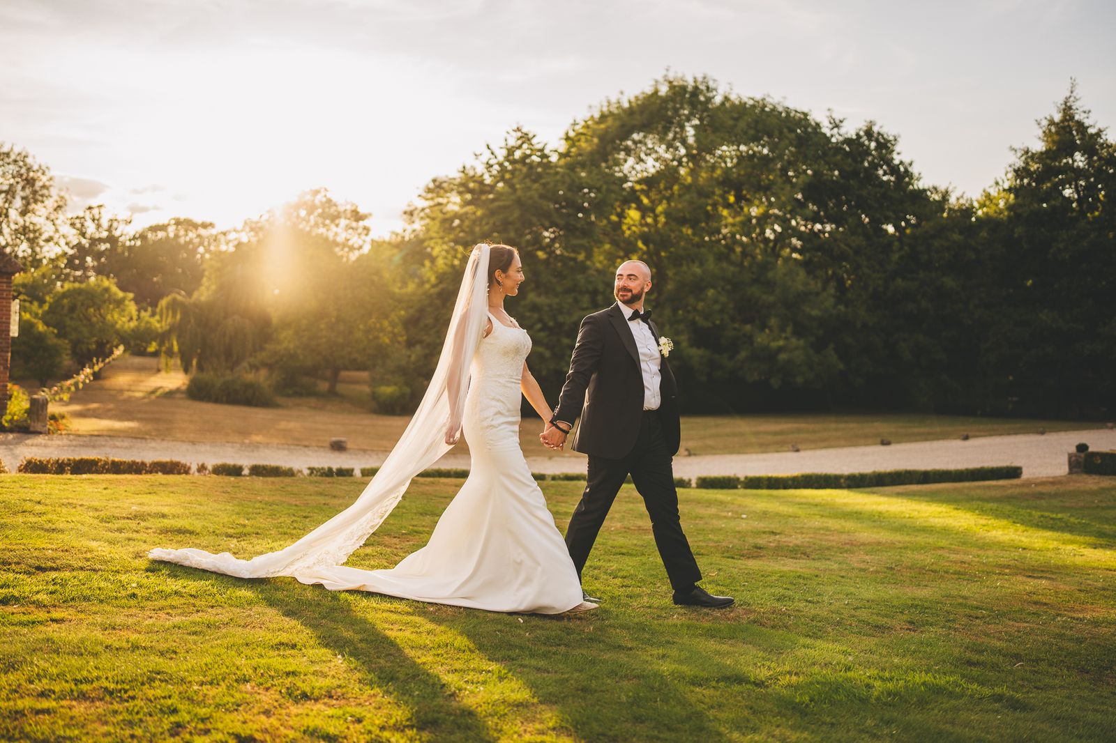 Bride and groom walking hand in hand across the lawn at sunset