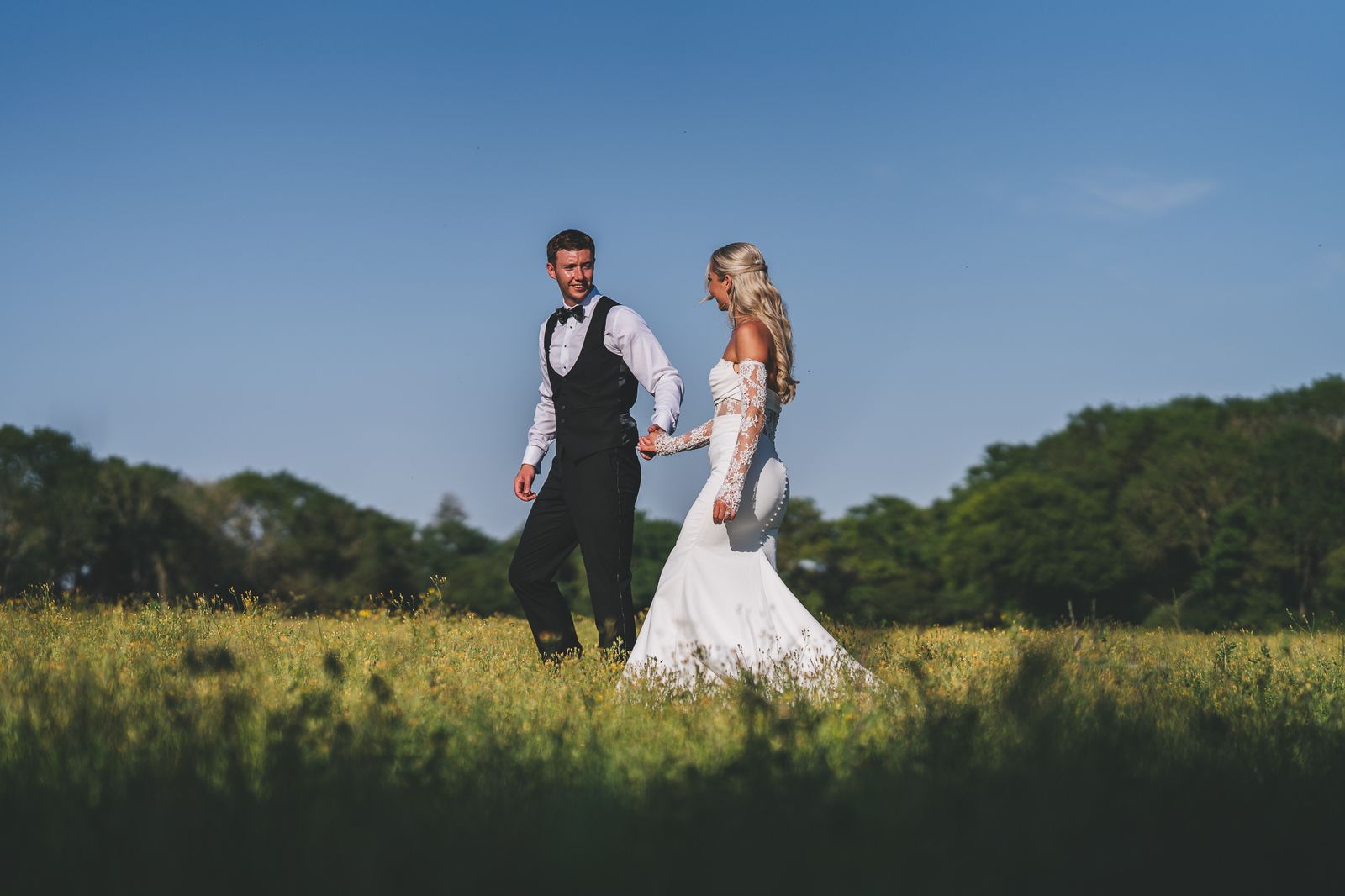 Bride and groom holding hands in a meadow under a blue sky